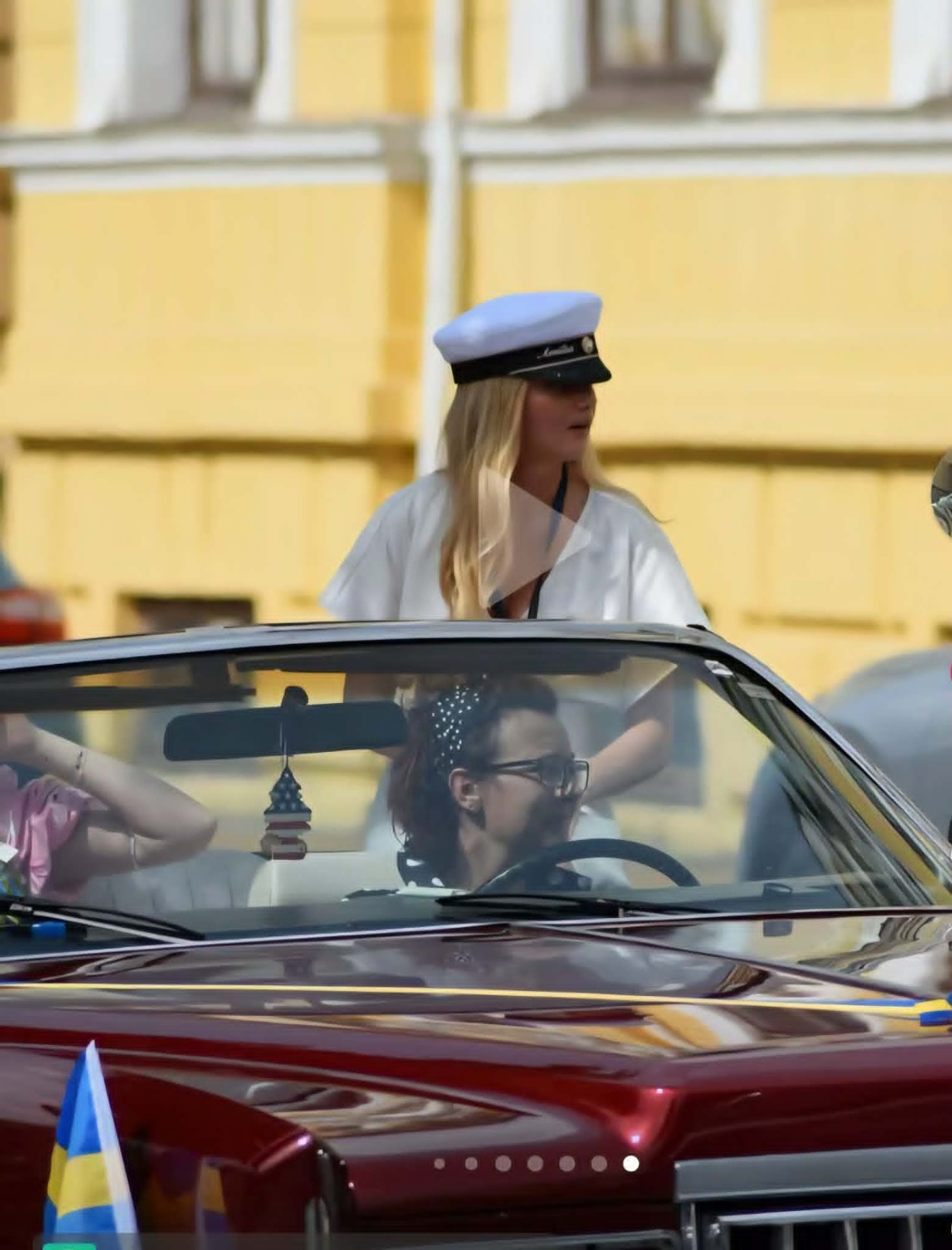 Student med studentmössa står upp i en vinröd Cadillac cabriolet