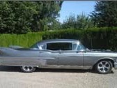 Silvergrå Cadillac 1958 i profil framför häck
