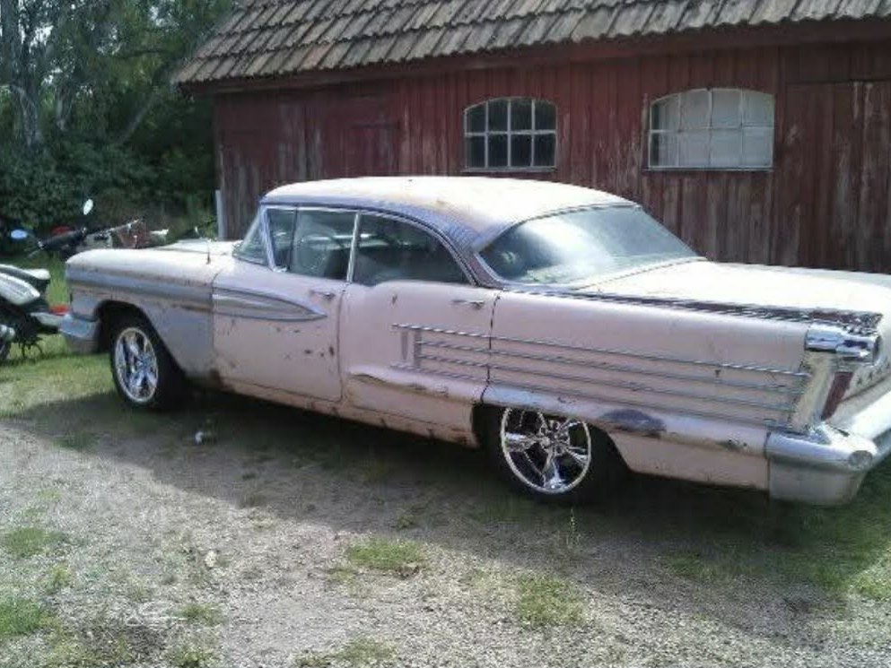 Rosa Cadillac 1958 i originalskick vid en röd lada